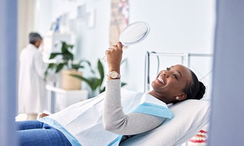 Woman smiling at reflection in handheld mirror