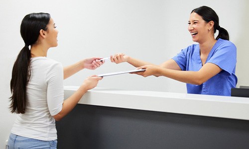 Smiling dental assistant handing patient form
