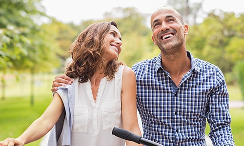 Couple smiling together outdoors after dental implant tooth replacement