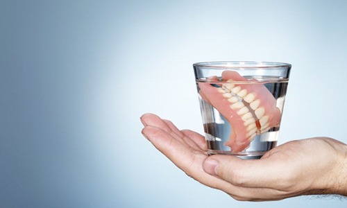 Outstretched hand holding dentures in Webster in glass of water