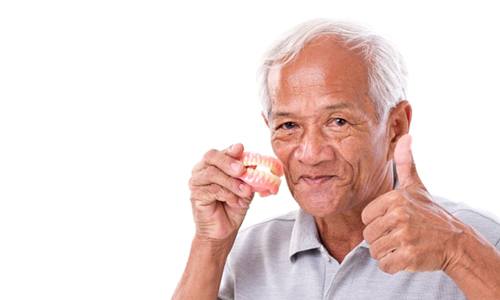 Man holding dentures in Webster smiles and gives thumbs up