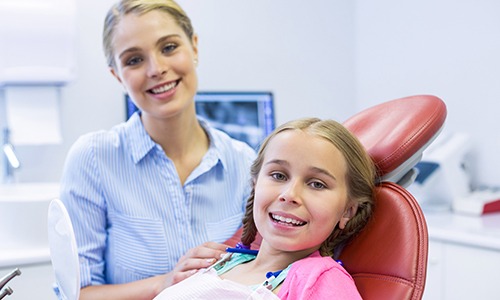 Young girl in dental chair smiling with dental team member