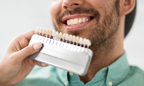 Dentist holding shades of veneers in Webster against patient's teeth