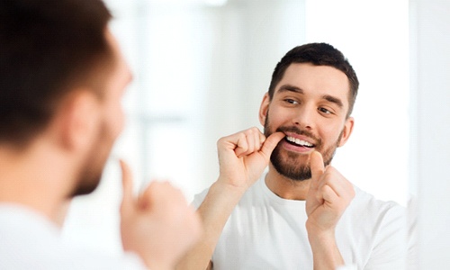Man smiling in mirror while flossing