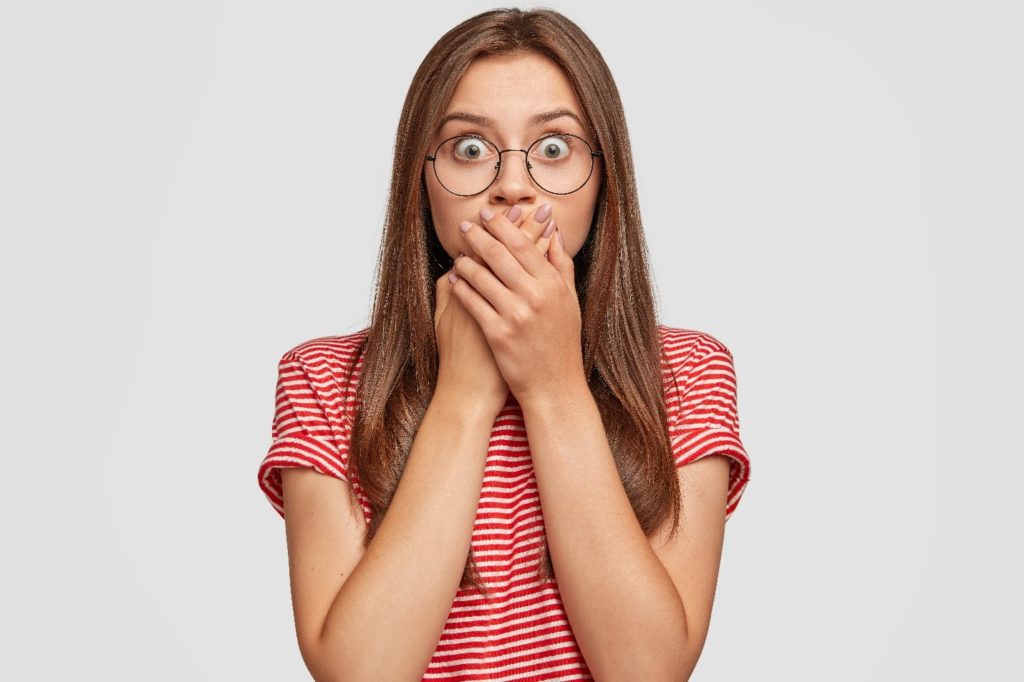 Woman with glasses covering her mouth in shock