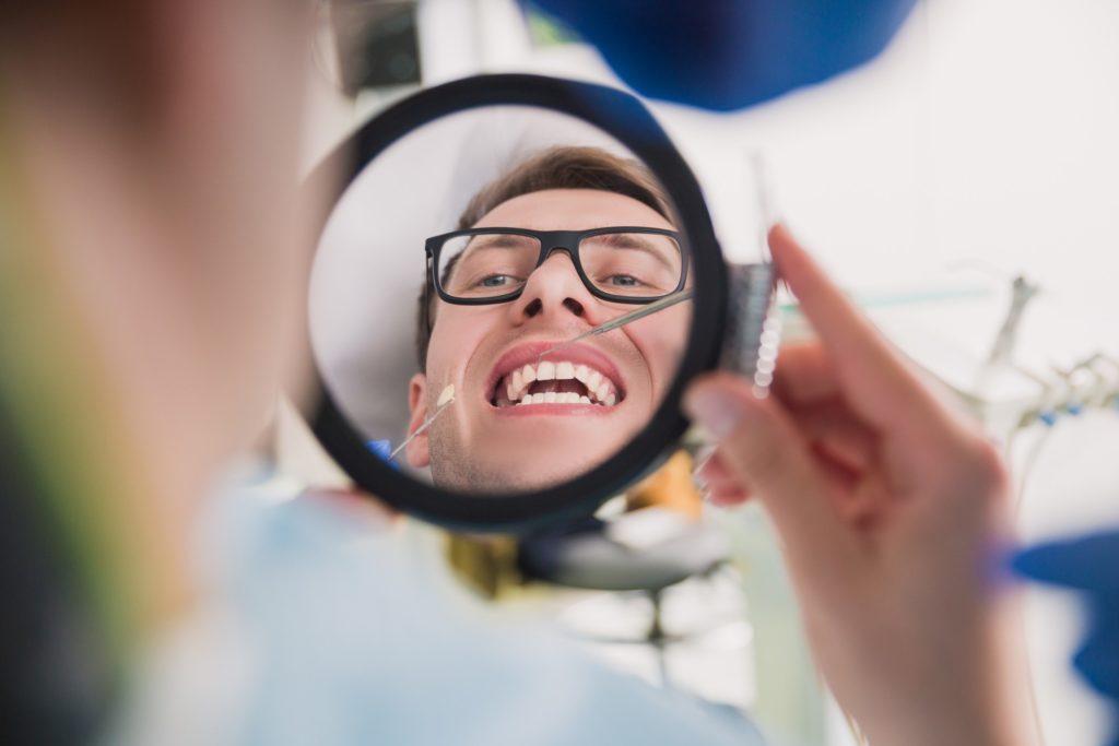 Man looking at teeth in dentist's mirror